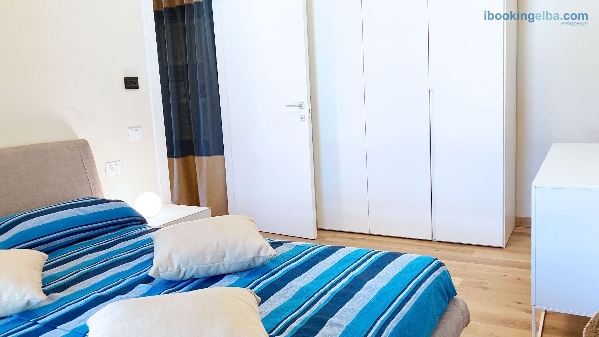 Ein Schlafzimmer mit Bett, Kissen, Nachttisch, Kleiderschrank und Schreibtisch.