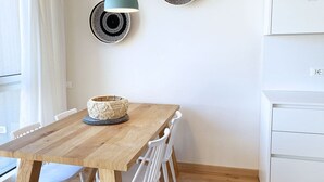 Una mesa de comedor de madera con un centro de mesa de mimbre, sillas blancas, una lámpara de pared y un armario blanco.