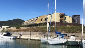 Un puerto deportivo con varias embarcaciones amarradas, un edificio de diseño arquitectónico singular y un paisaje montañoso al fondo.