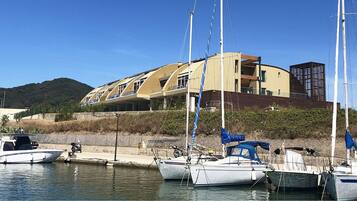 Un port de plaisance où sont amarrés plusieurs bateaux, un bâtiment doté d’une architecture originale et, au loin, un paysage vallonné.