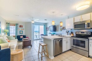 A modern kitchen with stainless steel appliances, a central island, and a dining area with a sofa and chairs. - Grand Beach 207 | Pool + Hot Tub + Gulf Views (Gulf Shores)