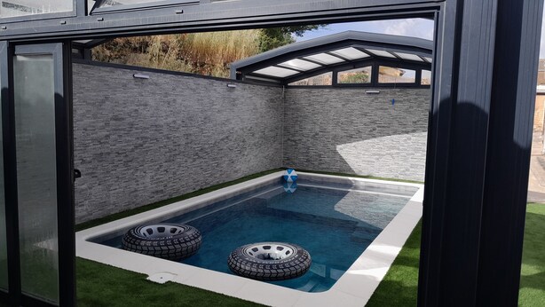 A modern outdoor pool area with a stone wall, a glass roof, and two tires as decorative elements. - Casa Totalmente Nueva, Para 16 Personas a 12 km de Burgos en un Pueblo Tranquilo (Villanueva-Matamala)