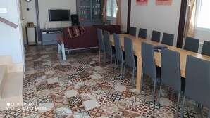 A dining area with a long table and chairs, a television, a cabinet with glass doors, and patterned floor tiles. - Casa Totalmente Nueva, Para 16 Personas a 12 km de Burgos en un Pueblo Tranquilo (Villanueva-Matamala)