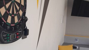 A dartboard mounted on a wall, a small table with a cup, and a couch with yellow cushions. - Casa Totalmente Nueva, Para 16 Personas a 12 km de Burgos en un Pueblo Tranquilo (Villanueva-Matamala)