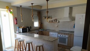A kitchen with a central island, wooden stools, a microwave, a stove, and a refrigerator. - Casa Totalmente Nueva, Para 16 Personas a 12 km de Burgos en un Pueblo Tranquilo (Villanueva-Matamala)
