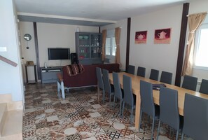 A dining area with a long table and chairs, a television, a cabinet with glass doors, and patterned floor tiles. - Casa Totalmente Nueva, Para 16 Personas a 12 km de Burgos en un Pueblo Tranquilo (Villanueva-Matamala)