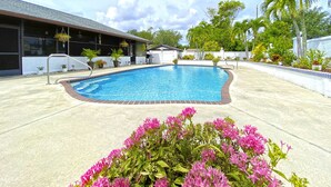 Une piscine bordée de briques, entourée d’une terrasse en béton et agrémentée de plantes en pot.
