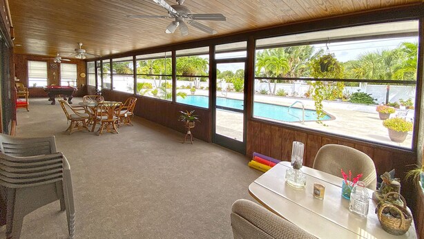 Un vaste espace intérieur avec vue sur la piscine, un plafond en bois et des meubles en osier.