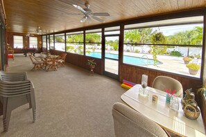 A spacious indoor area with a pool view, wooden ceiling, and wicker furniture. - Manatee Pocket Place (Stuart)