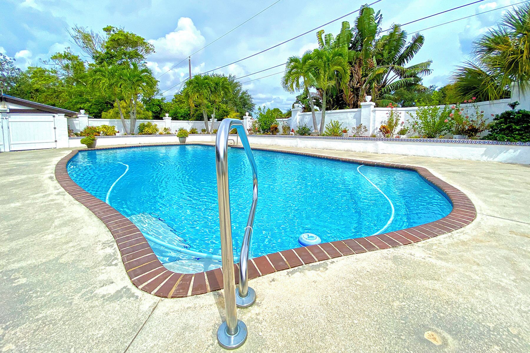 Piscina retangular com borda de tijolos e escada de metal.
