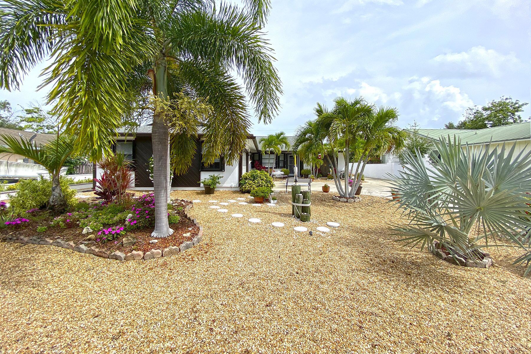 A landscaped garden with palm trees, a gravel pathway, and a building with a modern design.