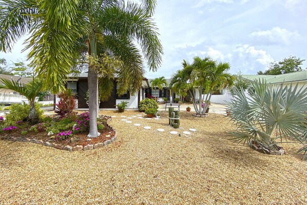A landscaped garden with palm trees, a gravel pathway, and a building with a modern design. - Manatee Pocket Place (Stuart)