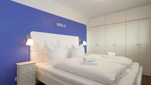 Een slaapkamer met een bed, witte nachtkastjes, een blauwe accentmuur en een kledingkast.
