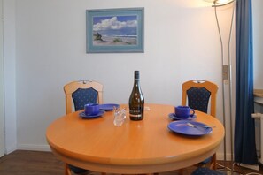 A round wooden table with two blue chairs, a bottle of wine, and blue plates and cups. - At Undine Beach, Germany (Sylt)