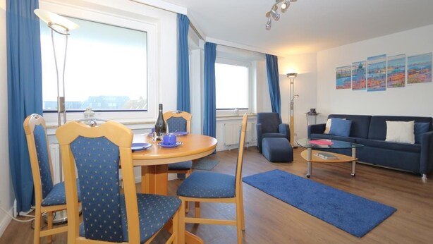 Een moderne woonkamer met een ronde houten tafel, blauwe fauteuils, een donkerblauwe bank en een glazen salontafel.