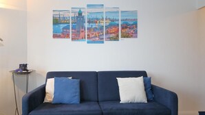 Een woonkamer met een donkerblauwe bank, twee kussens en een stadsgezicht aan de muur.