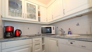 Een keuken met witte kastjes, een rode koffiezetapparaat, een magnetron en een fles afwasmiddel.