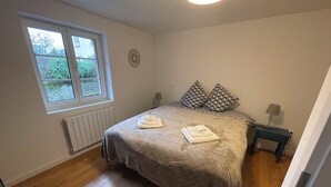 Een slaapkamer met een groot bed, twee kussens, een nachtkastje met een lamp, een raam met uitzicht en een radiator.
