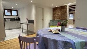 Een eethoek met een tafel gedekt voor twee personen, een keuken op de achtergrond en een bakstenen muur.