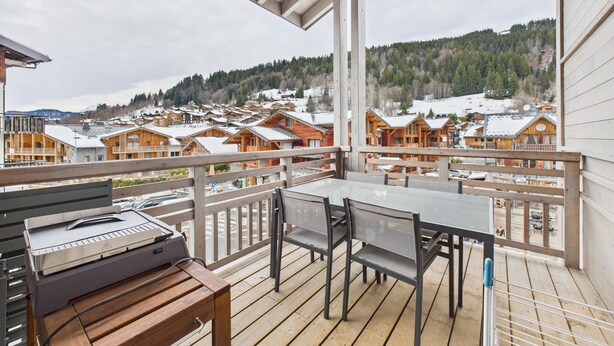 A wooden deck with a table and chairs, overlooking a snow-covered village with wooden buildings. - Cozy apartment in the heart of the village with terrace and garage - Les Gets (Les Gets)