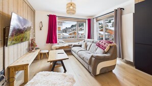 A cozy living room with a sofa, a wooden bench, a table, and a TV on the wall. - Cozy apartment in the heart of the village with terrace and garage - Les Gets (Les Gets)