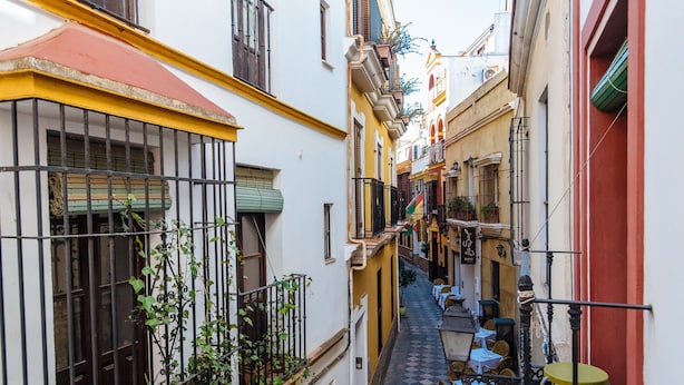 Une ruelle étroite avec des tables à l’extérieur, des plantes en pot et des balcons.
