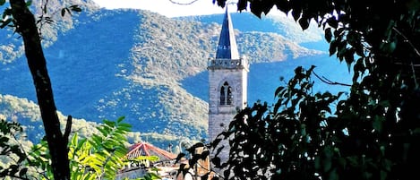 A church with a tall bell tower, surrounded by lush greenery and mountains in the background.