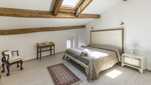 A bedroom with a skylight, a bed with a quilted bedspread, a bedside table with a lamp, a wooden bench, and a small table with a lamp. - "l'escapade"... Entre Lacs, mer et Montagnes (Hérépian)