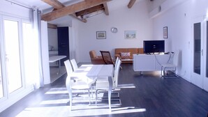 A modern kitchen with white cabinetry, a dining area with a white table and chairs, and a living area with a sofa and a television. - "l'escapade"... Entre Lacs, mer et Montagnes (Hérépian)