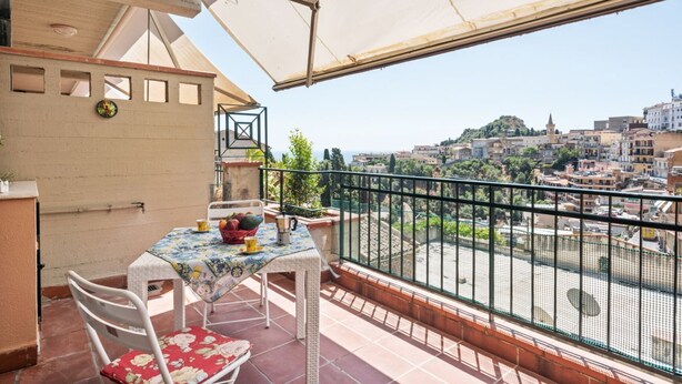 A balcony with a table and chairs, a view of a cityscape, and a decorative wall. - GuestHost - Comfortable 50 sqm apartment with terrace, able to accommodate up to 4 people, located on the fifth floor of a building with lift (NOT suitable for disabled people - 15 steps to access it). The property is located in a quiet area of ​​Tao (Taormina)