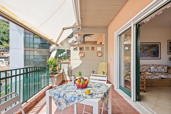 A balcony with a table, chairs, and a fruit basket.