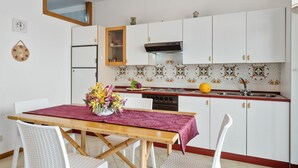 A kitchen with white cabinets, a wooden table, and a red tablecloth. - GuestHost - Comfortable 50 sqm apartment with terrace, able to accommodate up to 4 people, located on the fifth floor of a building with lift (NOT suitable for disabled people - 15 steps to access it). The property is located in a quiet area of ​​Tao (Taormina)