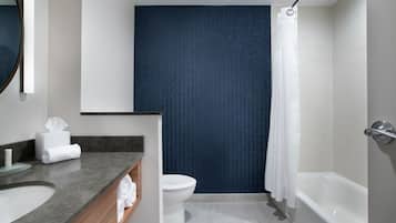 A modern bathroom with a grey countertop, a white sink, a toilet, and a bathtub.