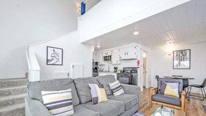 A modern apartment with a grey sofa, a dining table, and a kitchen in the background.