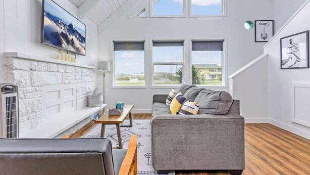 A modern living room with a fireplace, a grey sofa, and a large window offering a view of the outdoors.