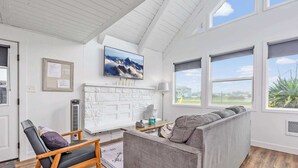 A cozy living room with a fireplace, a comfortable couch, and large windows offering a view of the outdoors.