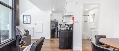 A modern kitchen with a central island, a dining area with a round table, and a view through a window.