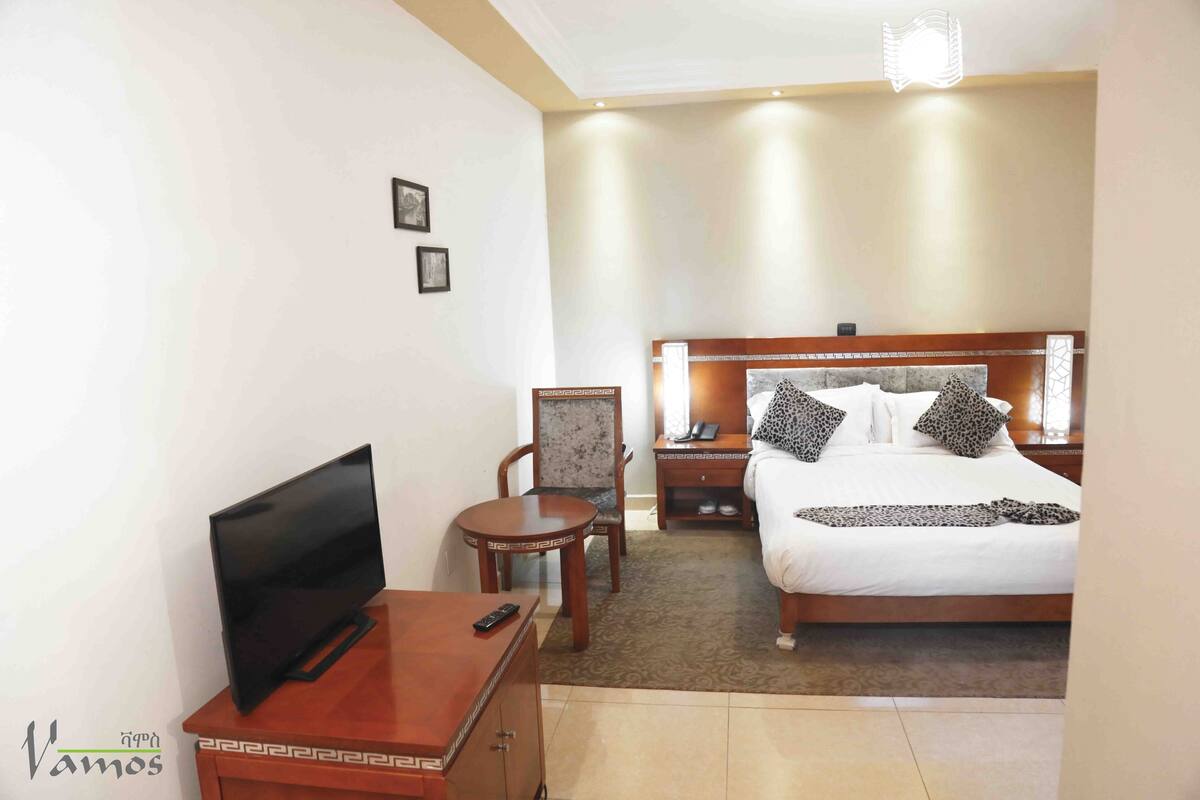 A hotel room with a bed, a TV, a desk, and a chair.