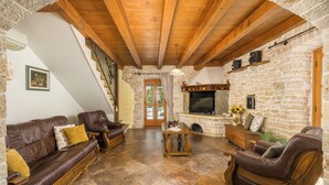 Ein gemütliches Wohnzimmer mit Kamin aus Stein, Ledersofas, Holzboden und einer Treppe.