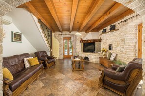 Ein gemütliches Wohnzimmer mit Kamin aus Stein, Ledersofas, Holzboden und einer Treppe.