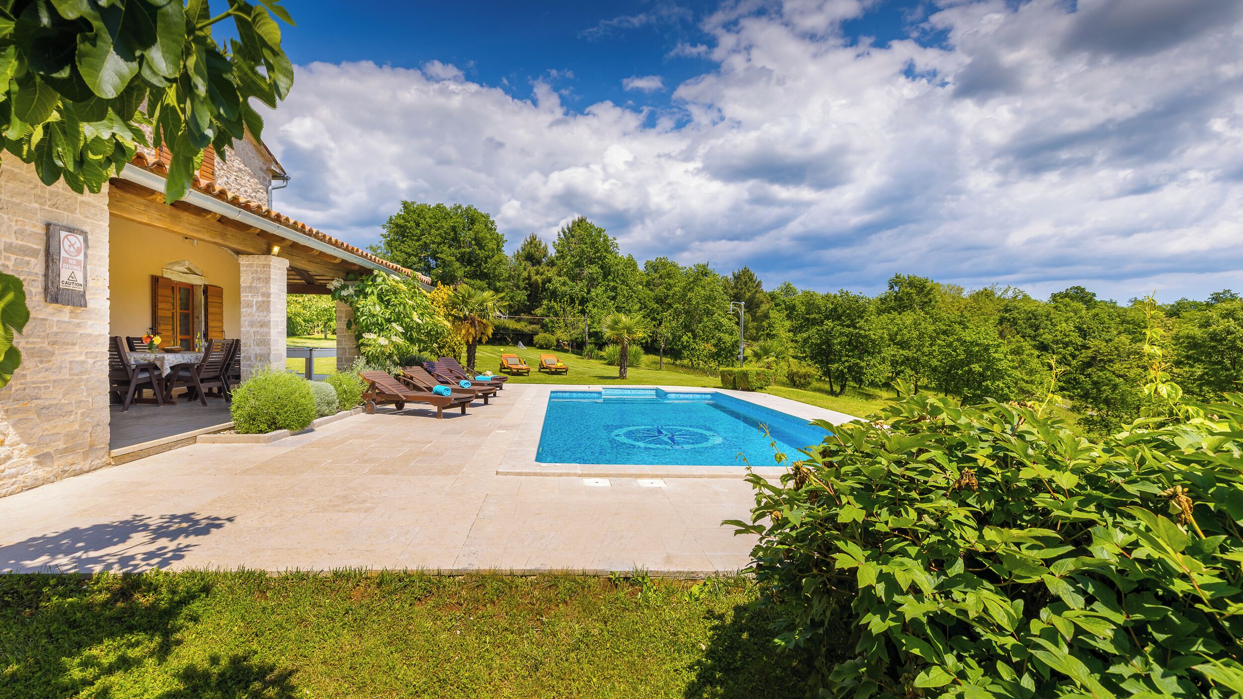 Una piscina con sillones de descanso, un edificio de piedra y abundante vegetación.