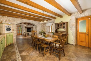 Une cuisine rustique aux murs de pierre, avec des poutres en bois et un coin repas comprenant des chaises et une table en bois.