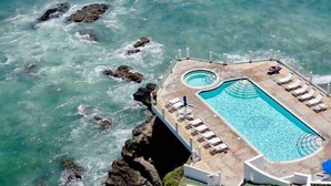 An aerial view of a rectangular pool with a curved section, surrounded by a deck with lounge chairs and a small pool area.