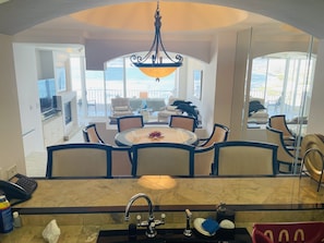 A dining area with a round table and chairs, a chandelier, and a view of the ocean through large windows. - OCEANFRONT w Amazing Views! Huge CLUB MARENA Rosarito Condo-SAFE Priv Beach/SURF (Rosarito)