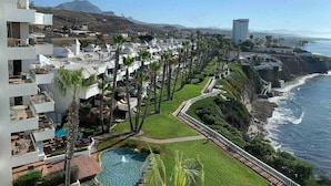 A resort with a pool, palm trees, and a view of the ocean.
