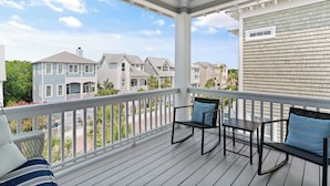 A covered porch with a white railing, two rocking chairs, and a small table. - Satilla Cottage - 4 Bedrooms in Coast Cottages (Saint Simons Island)