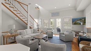A spacious living room with a staircase, comfortable seating, and a view of the outdoors. - Satilla Cottage - 4 Bedrooms in Coast Cottages (Saint Simons Island)