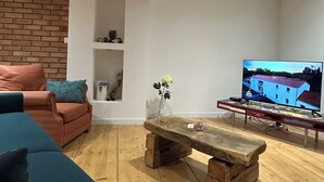 Una sala de estar con una mesa de centro de madera, un sofá, un televisor y una pared de ladrillo.