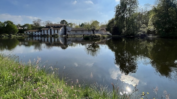 A serene lakeside setting with a white building featuring multiple windows and a balcony, surrounded by lush greenery and trees. - T1 on the shores of Lake Christus in Saint Paul Les Dax (Saint-Paul-lès-Dax)