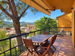 A balcony with a table and chairs, overlooking a town with buildings and a tree.